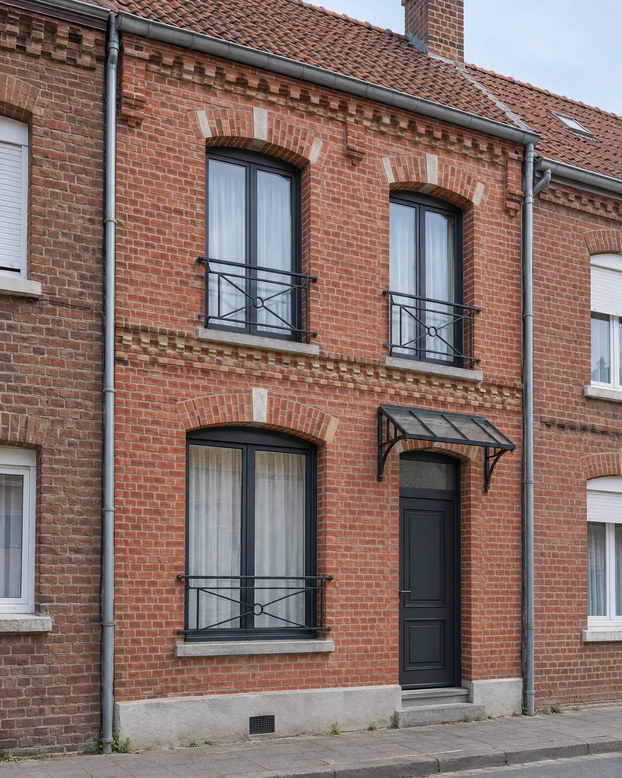Façade de maison en brique avec garde-corps de fenêtre et marquise en acier noir
