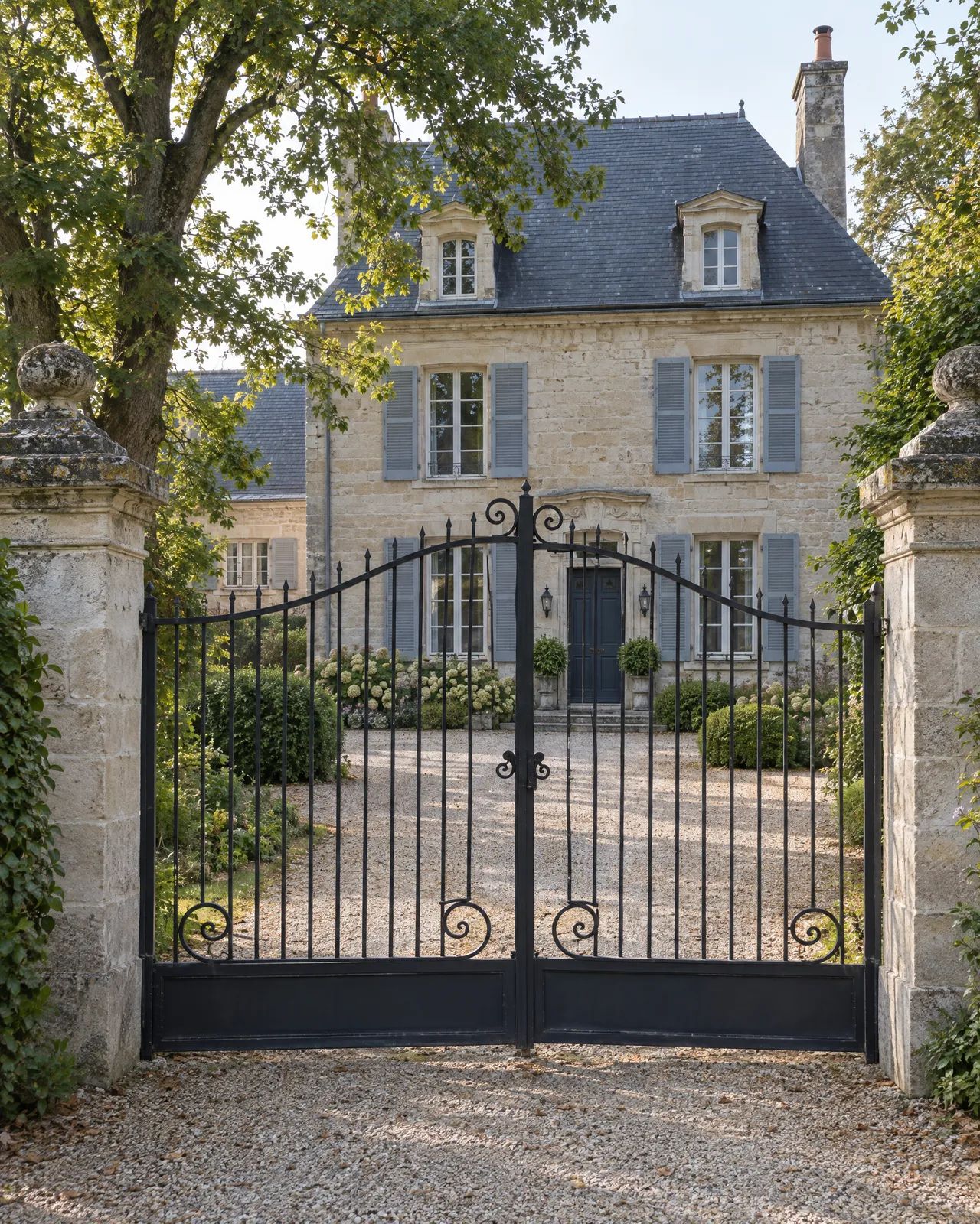 Portail en fer forgé noir à volutes devant une maison en pierre