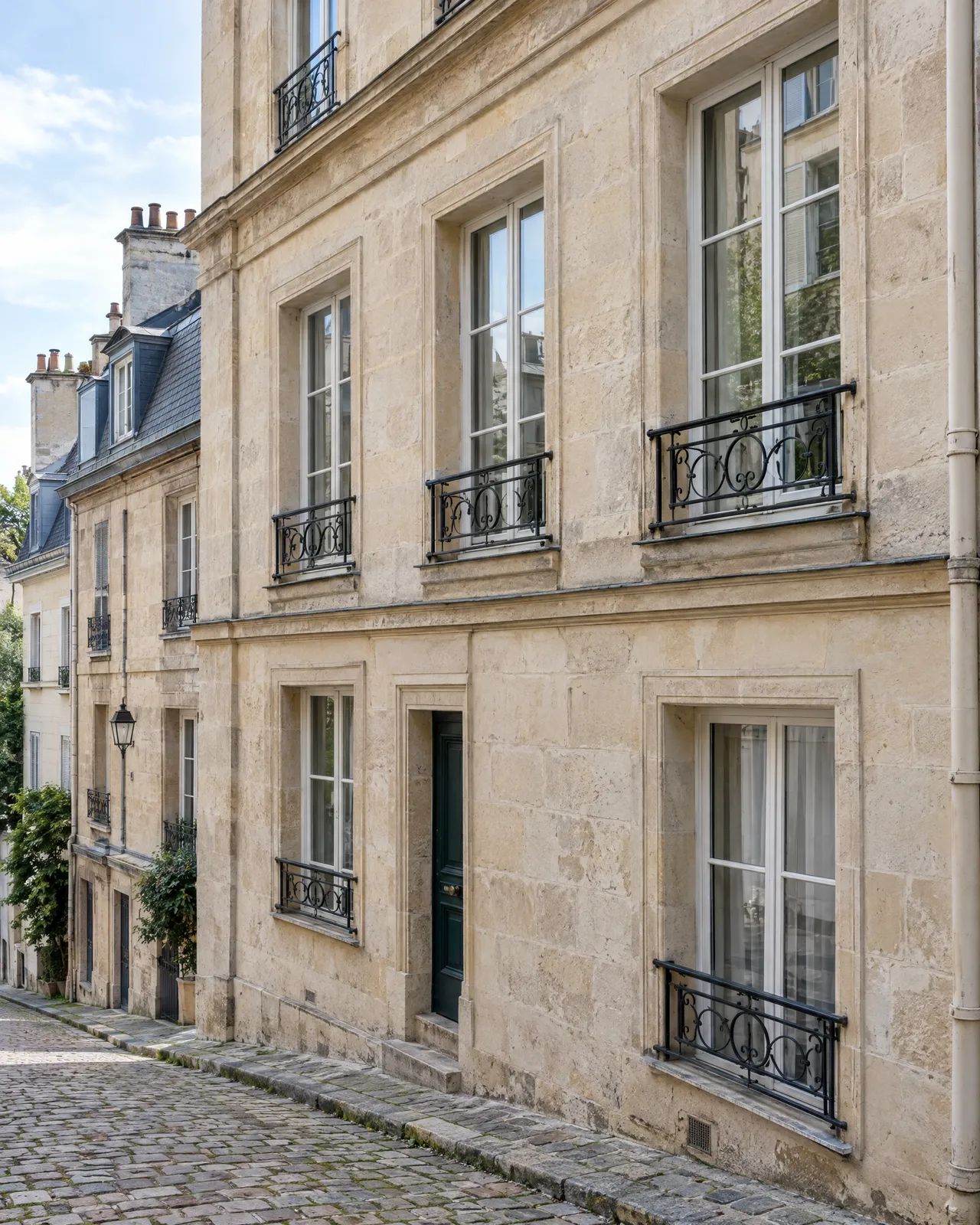 Façade en pierre avec garde-corps de fenêtre en fer forgé noir, dans une ruelle pavée